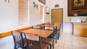 A dining area with wooden tables and chairs, a kitchen area with a microwave, and decorative wall art including a horse silhouette and a framed picture. - Super 8 by Wyndham Abilene KS (Abilene)