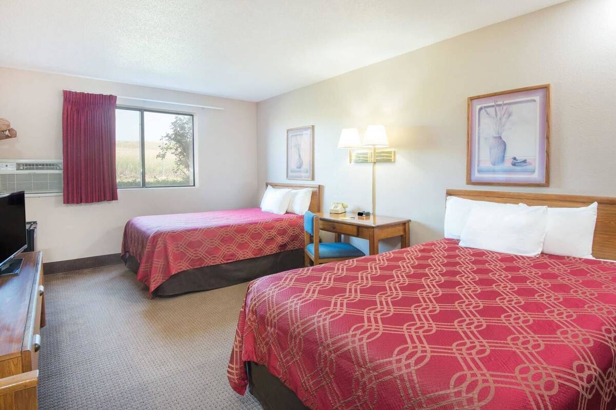 A hotel room with two beds, a desk, a chair, a TV, and a window with curtains.