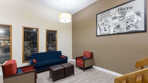 Een woonkamer met een blauwe bank, twee fauteuils, een houten salontafel en een groot schilderij in een lijst aan de muur.