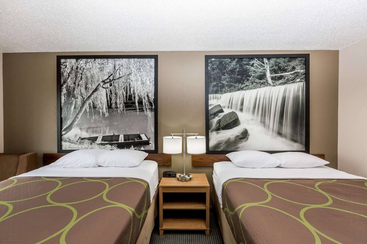 Een hotelkamer met twee bedden, een nachtkastje met een lamp en twee ingekaderde foto’s van watervallen.
