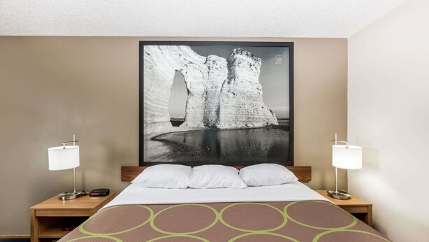 Een hotelkamer met een bed, twee nachtkastjes, een groot beeld in een lijst aan de muur, en twee lampen.