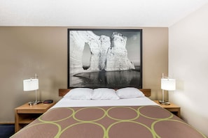 Habitación de hotel con una cama, dos mesitas de noche, un cuadro grande en la pared y dos lámparas.