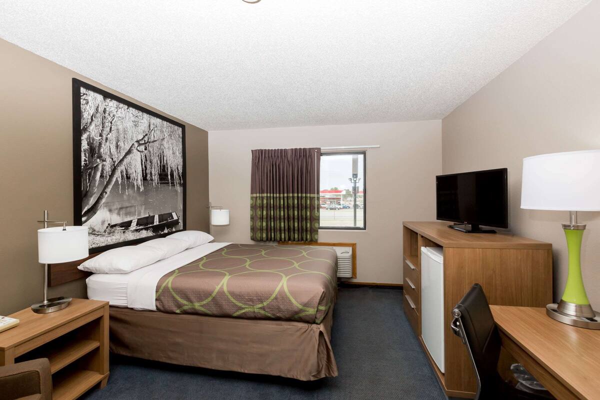 Hotelkamer met een bed, bureau, televisie, lamp en raam met gordijnen.