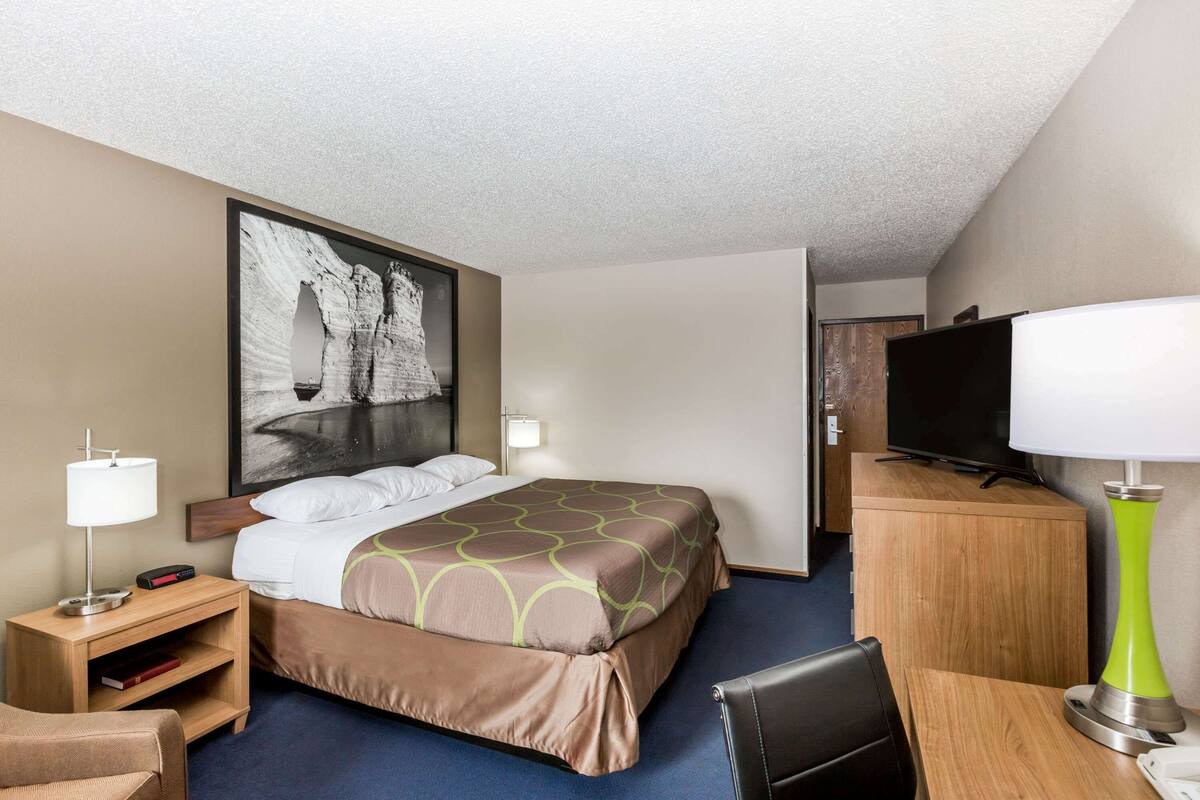 Een hotelkamer met een bed, een bureau, een televisie en een groot schilderij aan de muur.