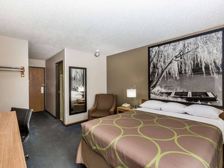 Une chambre d’hôtel avec un grand lit, un bureau, une chaise, une table de chevet avec une lampe et un grand tableau encadré au mur.