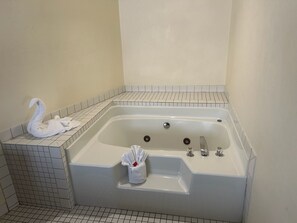Een badkamer met een bad, een handdoek in de vorm van een witte zwaan, en een witte handdoek op de vloer.