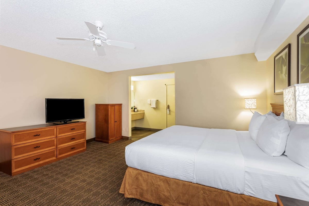 A hotel room with a bed, a television, a wardrobe, and a ceiling fan.