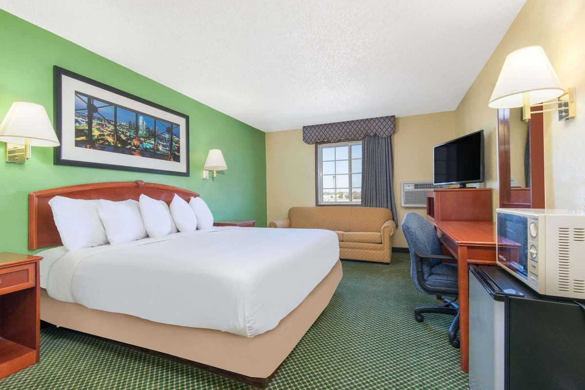 A hotel room with a large bed, a sofa, a desk with a computer, and a TV.