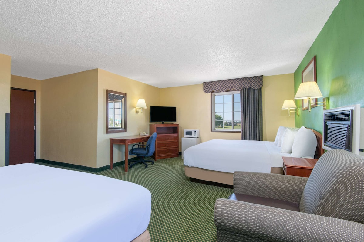 A hotel room with two beds, a desk with a chair, a television, and two lamps.