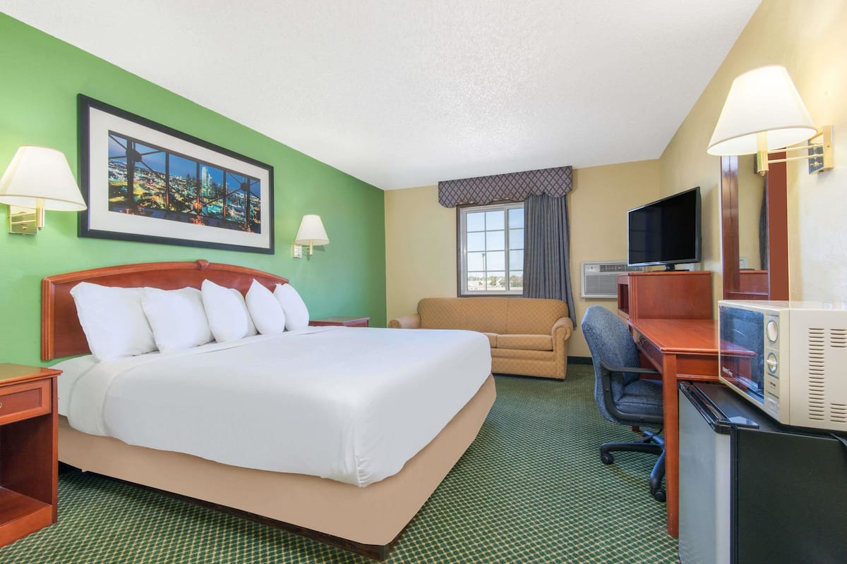A hotel room with a large bed, a sofa, a desk with a computer, a TV, and a picture on the wall.