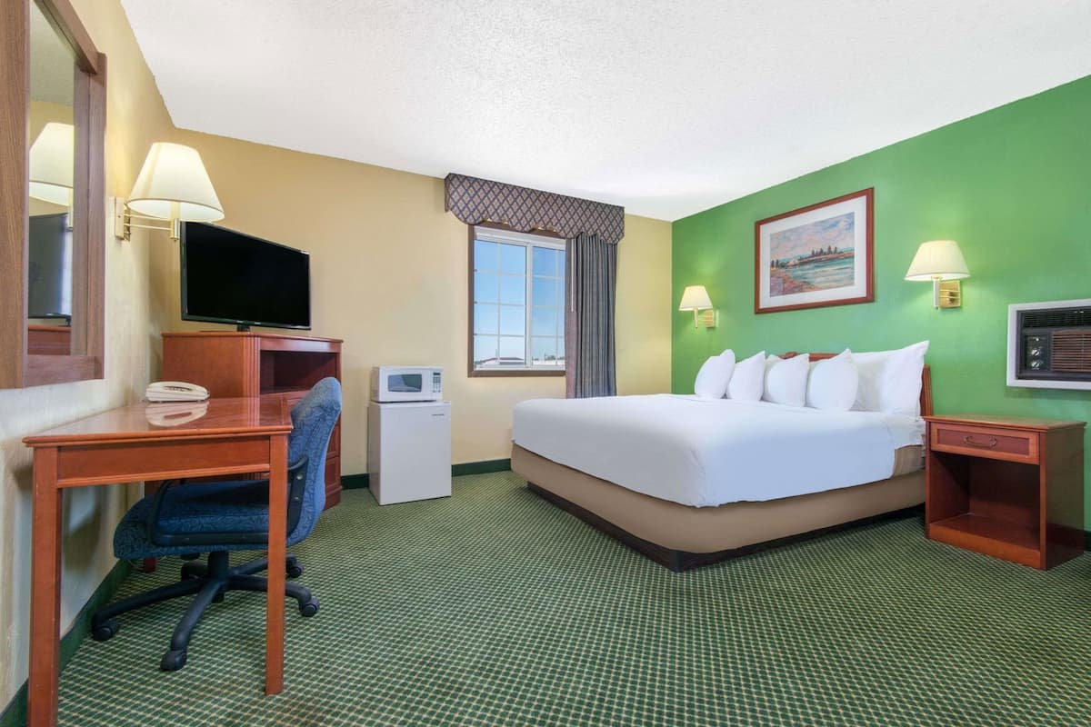 A hotel room with a bed, desk, chair, television, microwave, and a window with curtains.