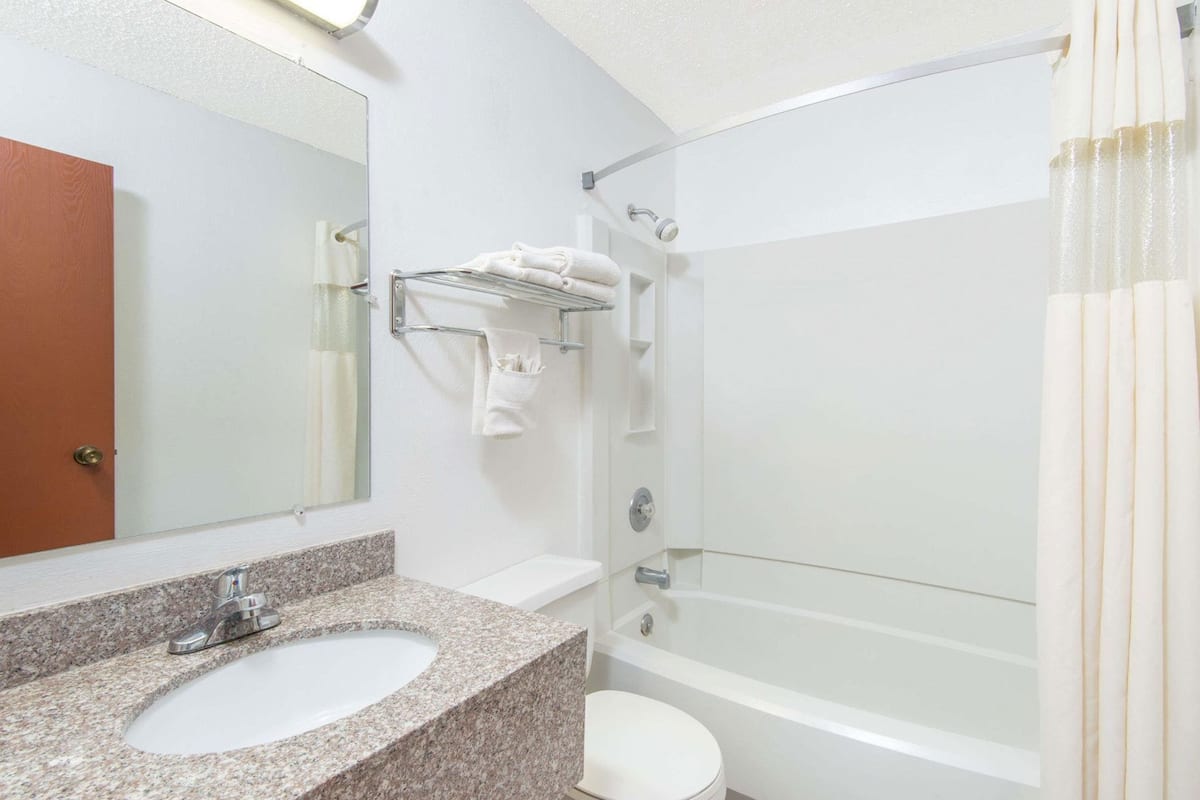 A bathroom with a granite sink, a toilet, a bathtub, and a shower.