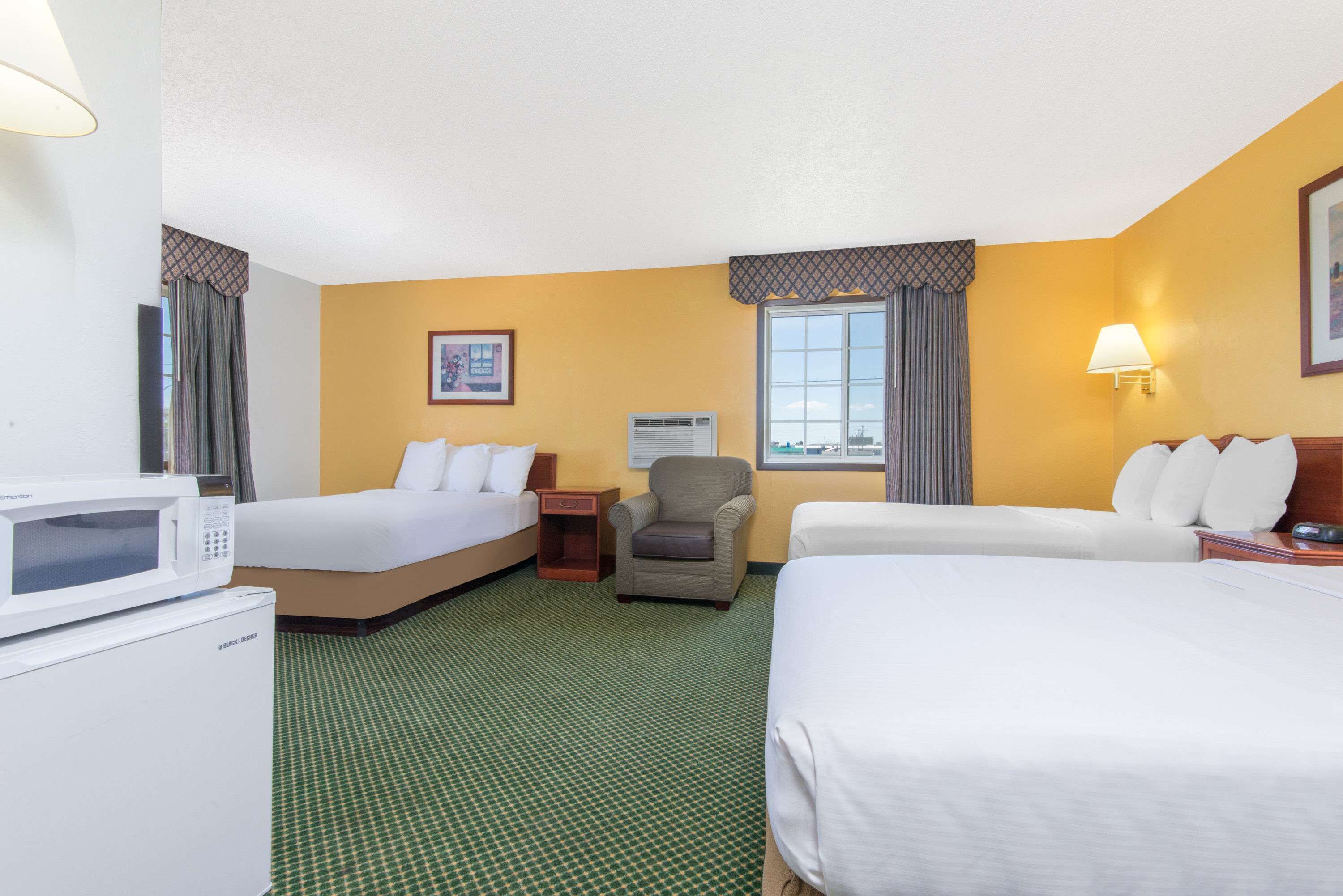 A hotel room with two beds, a microwave, a chair, a nightstand, and a window with curtains.