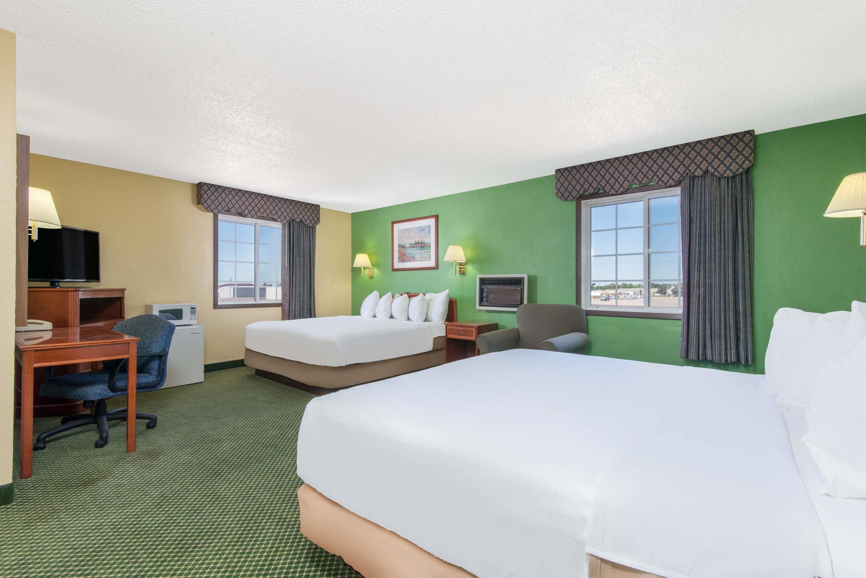 A hotel room with two beds, a desk with a computer, a chair, a TV, and a microwave.