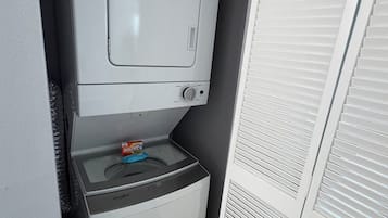 Een kleine wasruimte met een wasmachine en droger, een klein raam en een witte deur.