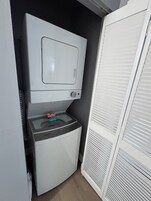 Uma lavanderia compacta com máquina de lavar e secadora, uma pequena janela e uma porta branca.