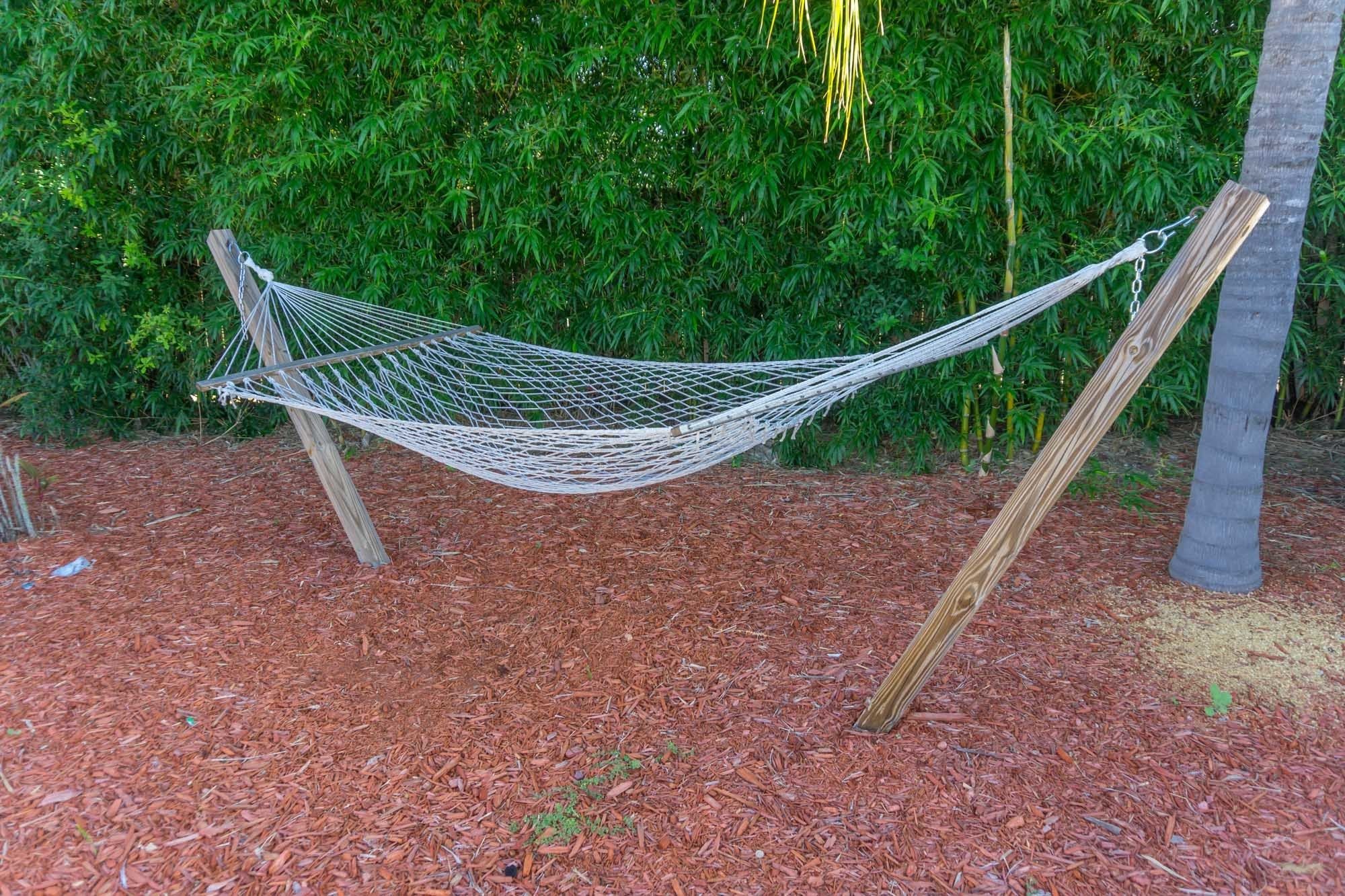 A hammock tied between two wooden posts in a garden with a dense green hedge in the background.
