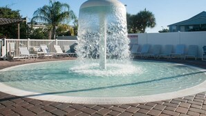 A circular pool with a central water fountain, surrounded by lounge chairs and a white fence.
