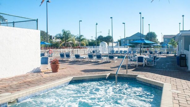 A pool area with lounge chairs and umbrellas, surrounded by a fence and buildings.