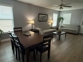 Uma sala de estar com uma mesa de jantar, dois sofás, um ventilador de teto e um quadro na parede.