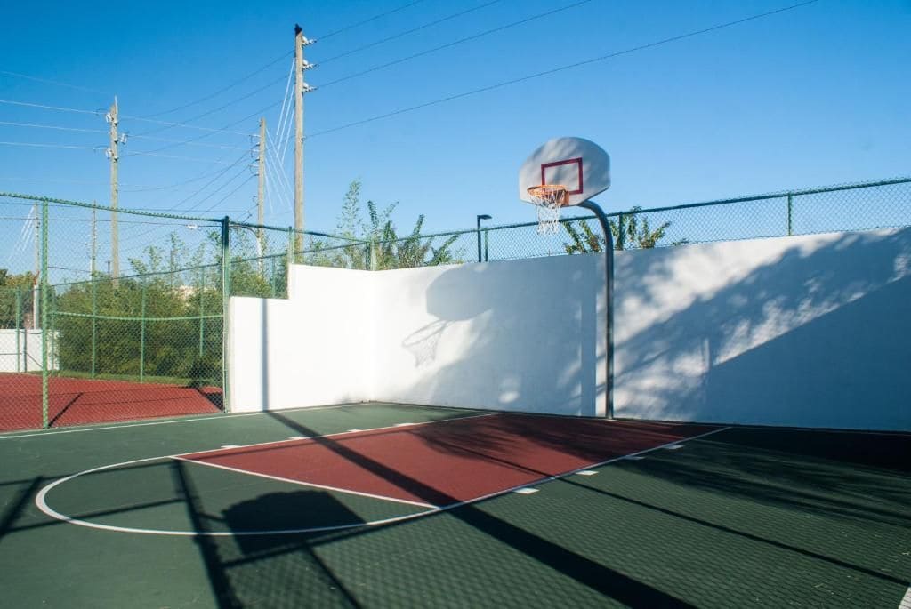 Een buitenbasketbalveld met een hek van gaas, een basketbalring en een heldere lucht.