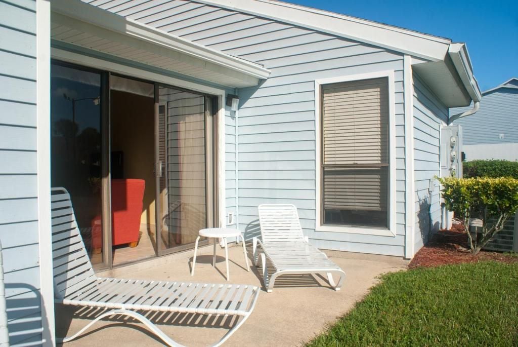 Una casa con un patio techado que incluye dos sillones y una mesita.