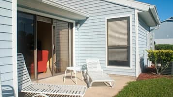 Una casa con un patio techado que incluye dos sillones y una mesita.