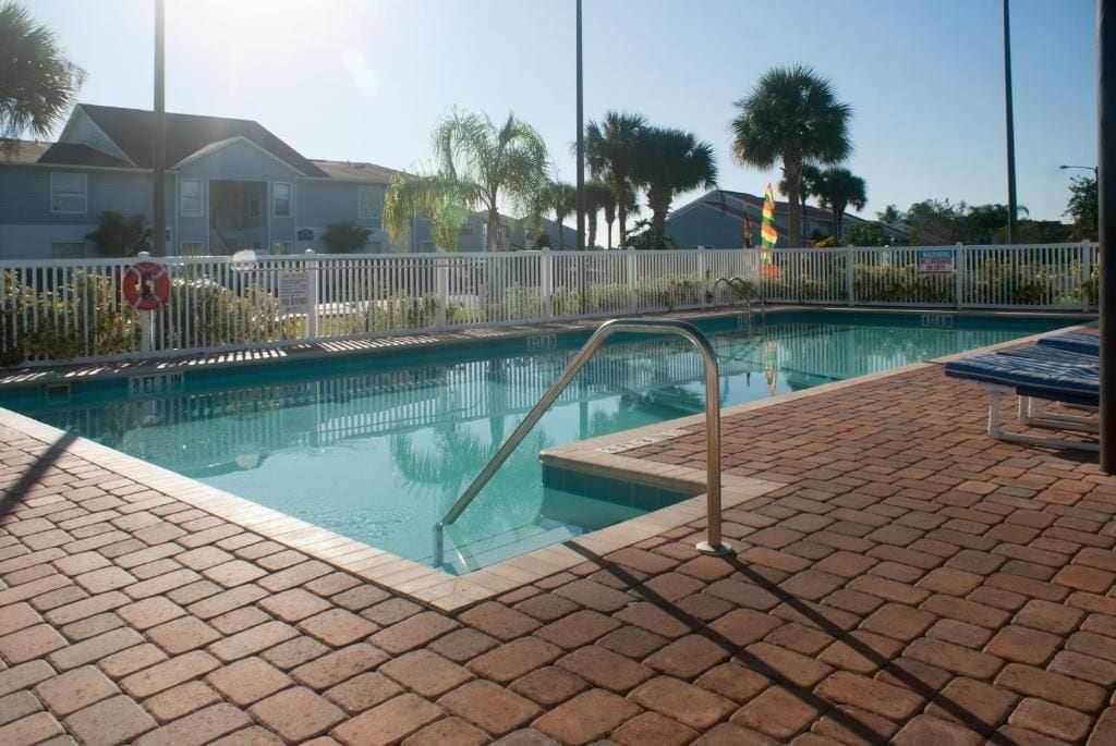 A swimming pool with a white fence, a lifeguard stand, and a brick patio.