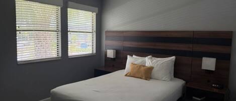 A bedroom with a bed, two windows with blinds, a ceiling fan, and a wooden headboard.
