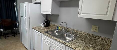 A kitchen with white cabinets, a granite countertop, a stainless steel sink, and a refrigerator.