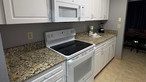 A kitchen with white cabinets, a microwave, a stove, and a blender on the counter.