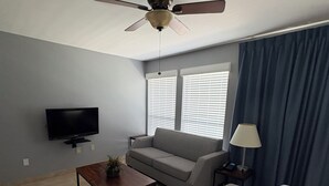 A living room with a ceiling fan, a television, a sofa, a coffee table, and a lamp.