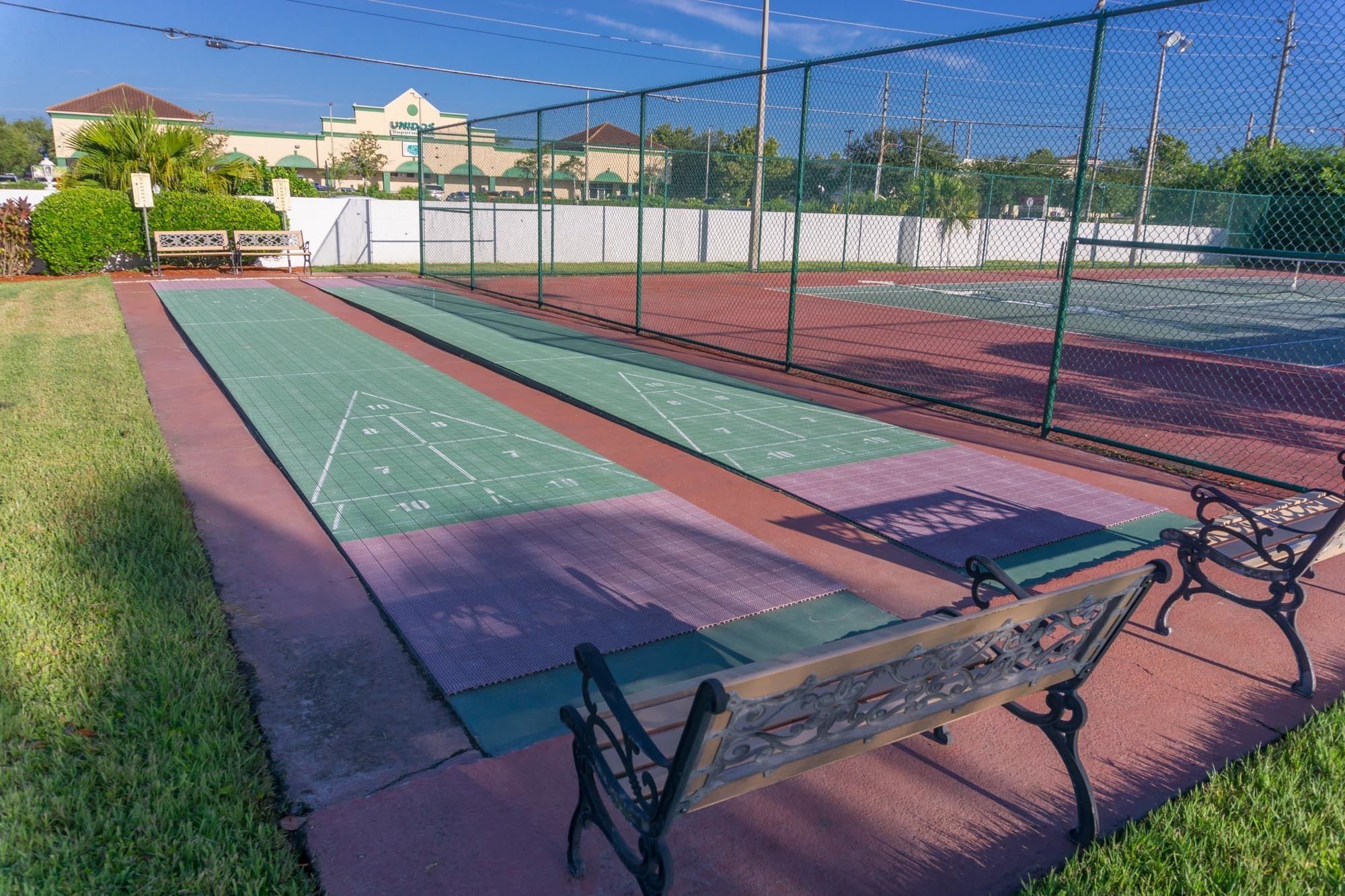 Una cancha de tenis con superficie verde y roja, rodeada por una cerca de malla metálica.