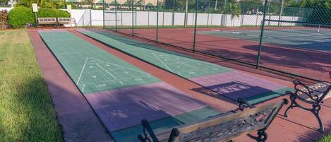 Una cancha de tenis con superficie verde y roja, rodeada por una cerca de malla metálica.