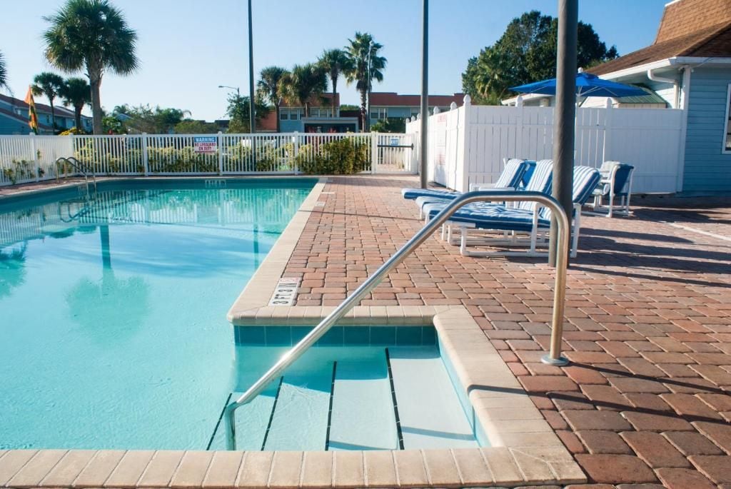 A swimming pool with a metal ladder, surrounded by a brick patio, and blue lounge chairs.