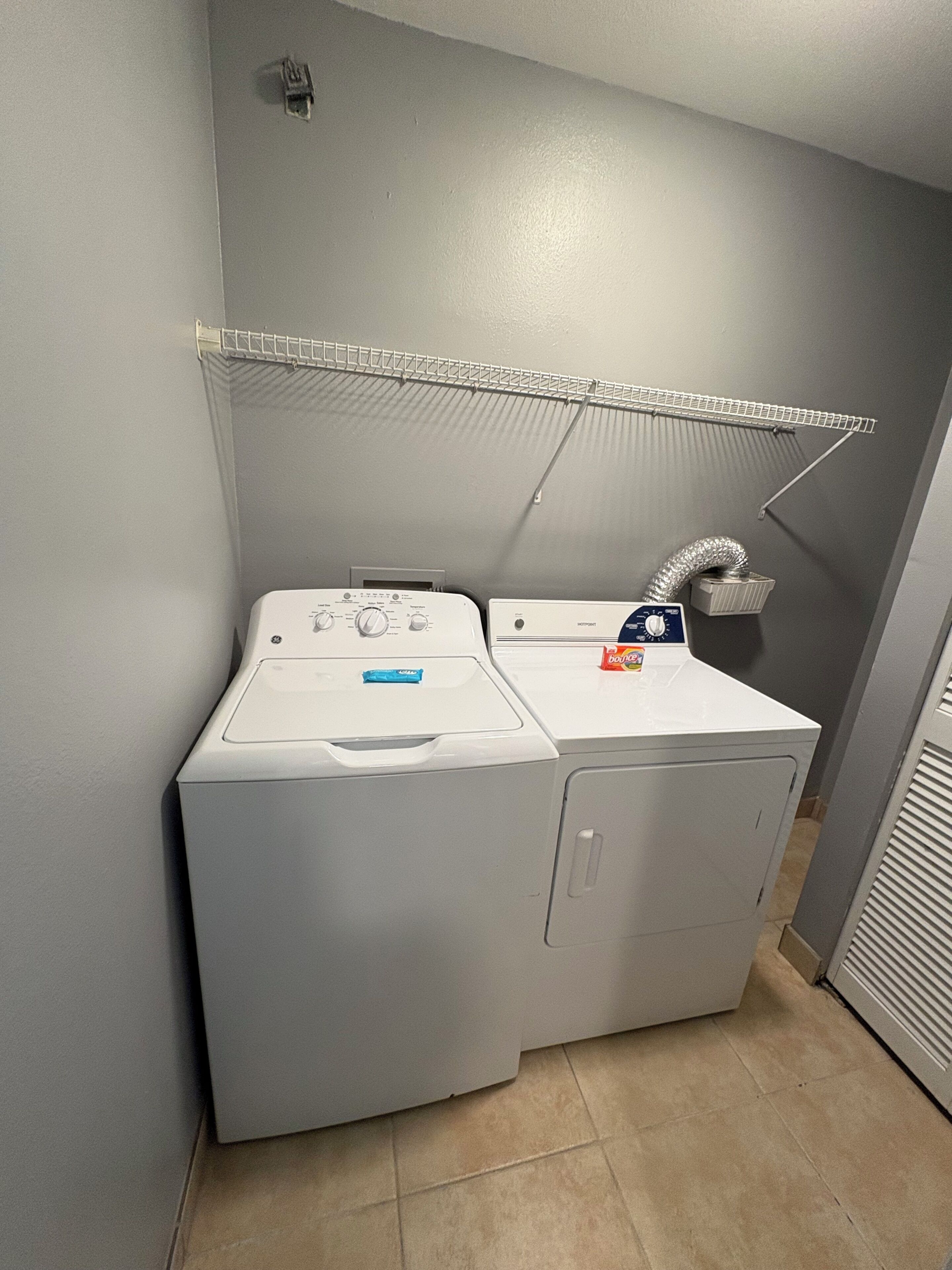 Een wasruimte met een voorlader wasmachine en droger, een droogrek en een ventilatieslang.