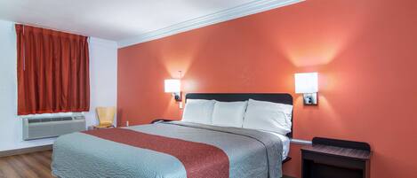 Habitación de hotel con cama, una silla, una mesita de noche y un calentador instalado en la pared.