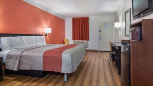 Una habitación de hotel con una cama, un escritorio, un televisor y una puerta.
