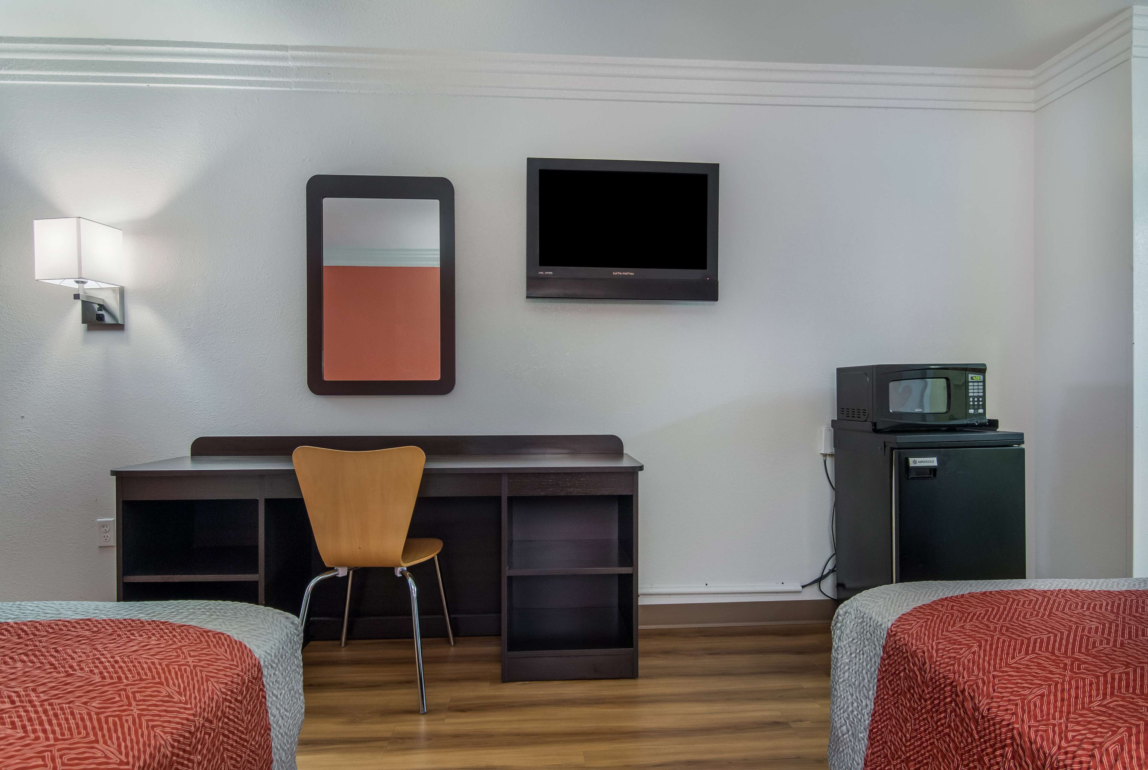 Hotellihuone, jossa on kaksi sänkyä, työpöytä tuolilla, televisio, mikroaaltouuni ja pieni jääkaappi.