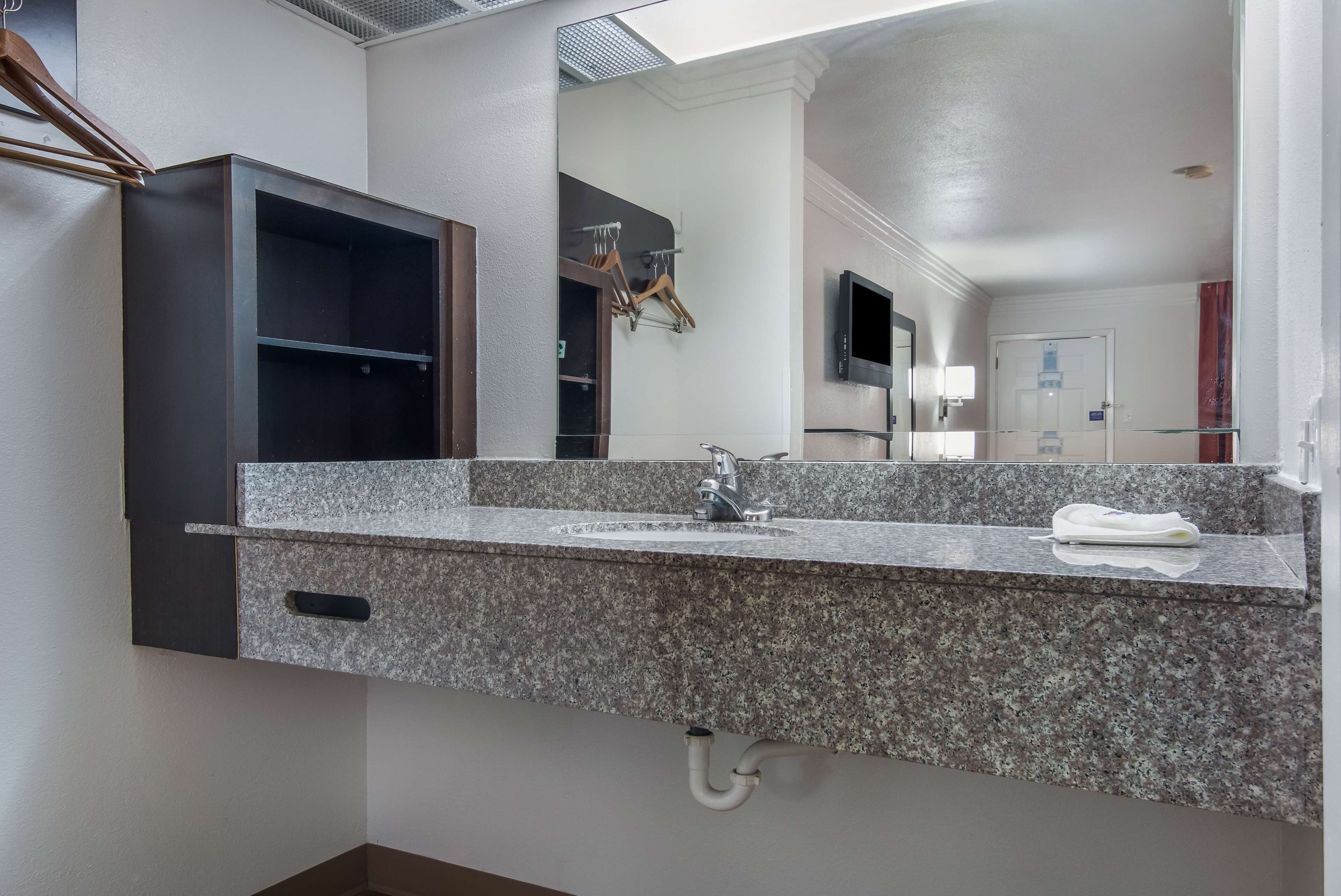 A bathroom with a granite countertop sink, a mirror, and a dark wooden cabinet.
