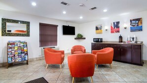 Zona de recepción de un hotel con una televisión de pantalla plana, un atril para revistas y una estación de café.