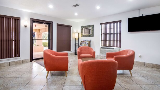 Un vestíbulo amplio con suelo de baldosas, un mostrador de recepción y una zona de estar con cuatro sillones naranjas.