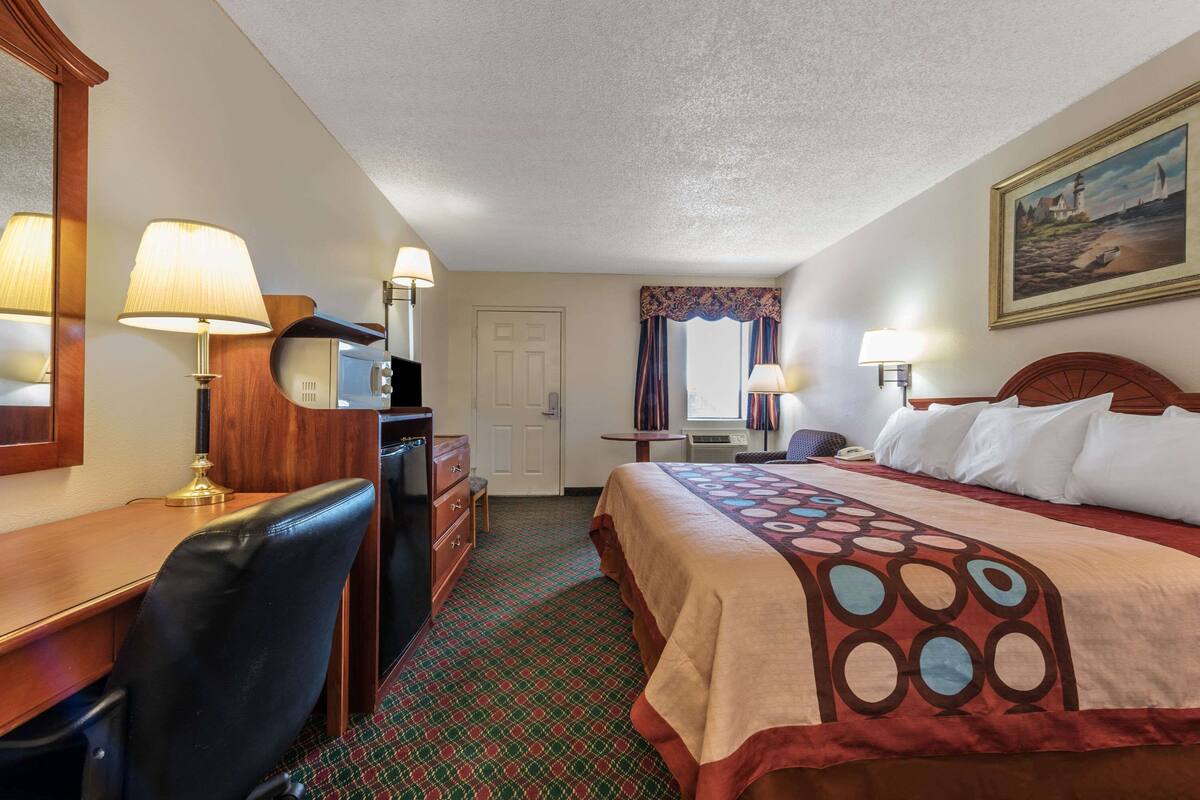 A hotel room with a bed, desk, chair, and a television.