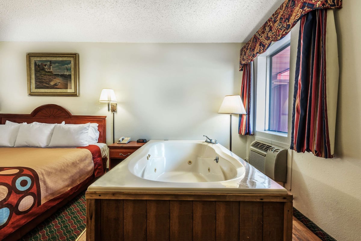 A hotel room with a large bed, a separate sitting area, a bathtub, and a window with curtains.