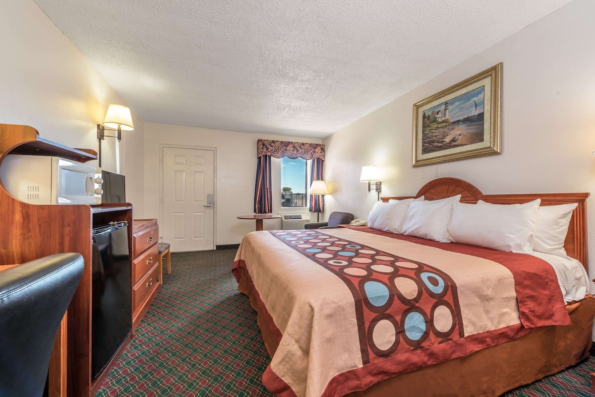 A hotel room with a bed, a desk, a chair, a dresser, and a painting on the wall.