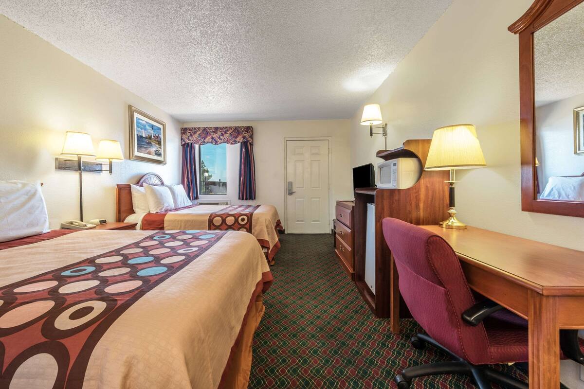 A hotel room with two beds, a desk, a chair, a dresser, and a television.