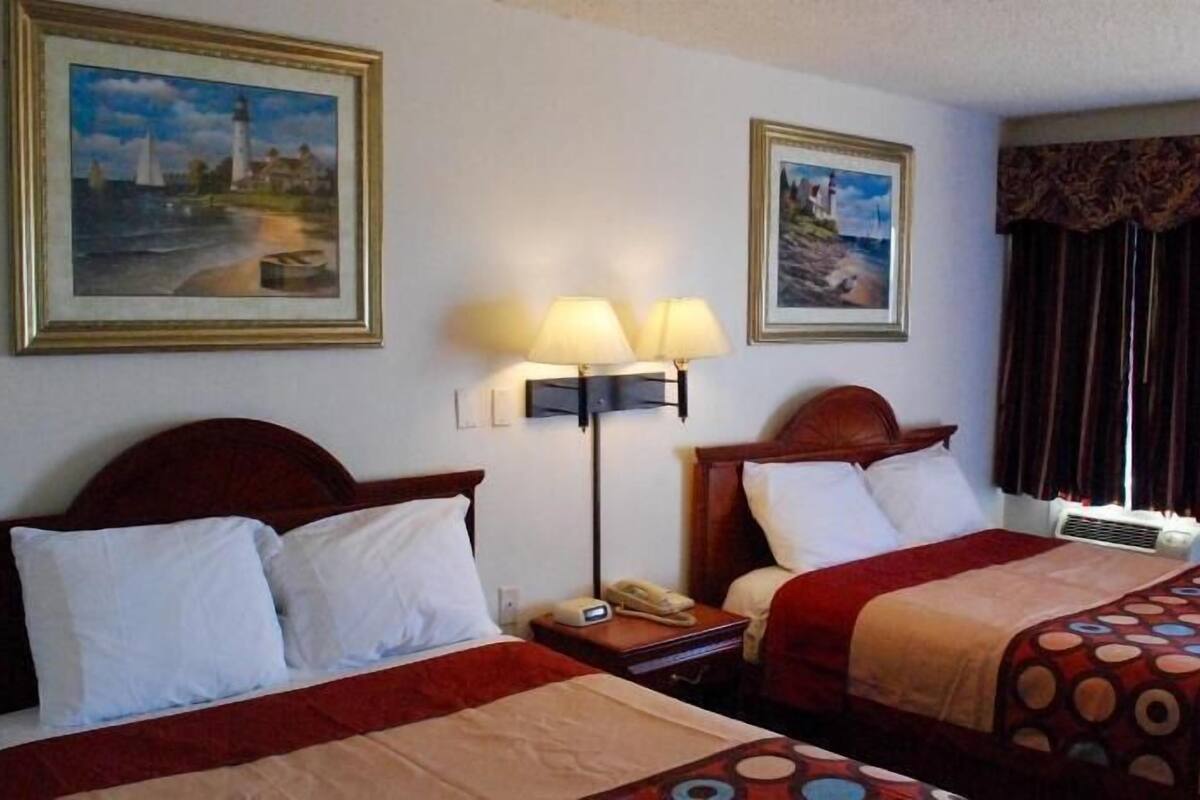 A hotel room with two beds, a nightstand with a telephone, wall-mounted lamps, and two framed pictures.