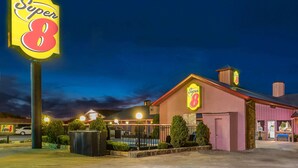 Un motel Super 8 amb un senyal de neon ben visible, una àrea de pàrquing tancada i un edifici amb façana rosa.