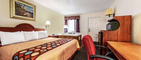 A hotel room with a bed, desk, chair, lamp, and a painting on the wall.