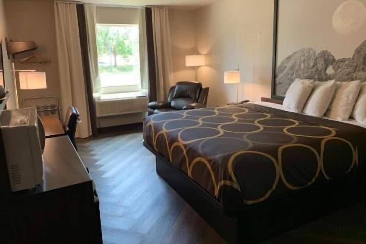 A hotel room with a bed, a desk, a chair, two lamps, and a window with curtains.